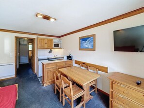 A compact kitchen with wooden cabinets, a microwave, and a sink. There's a dining table with chairs and a small wooden dresser. - Pleasant 2 rooms, 4 pers, south, Les Bruyères (Les Menuires)