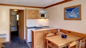 A compact kitchen with wooden cabinets, a microwave, and a dining area with a table and chairs. - Pleasant 2 rooms, 4 pers, south, Les Bruyères (Les Menuires)