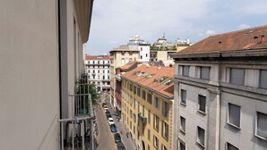 A narrow street with buildings on both sides, a clear sky, and a few cars and pedestrians. - notaMi - Cinque Vie Top Floor City Center (Milan)