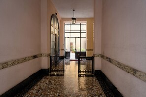 A hallway with a tiled floor, a large arched window, and a black gate.