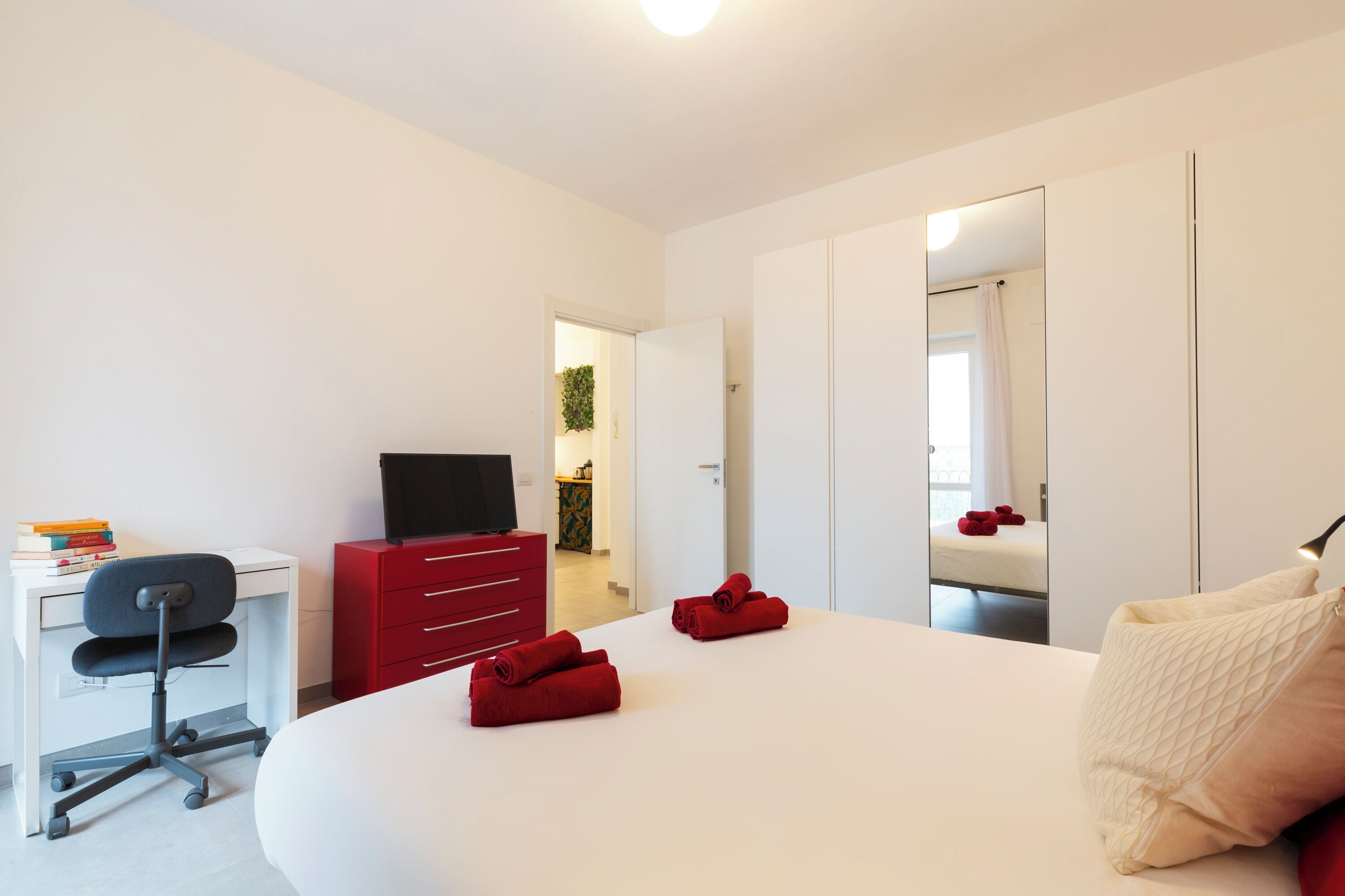 Una habitación de hotel moderna con una cama grande, un escritorio con una silla, un aparador rojo y un televisor.