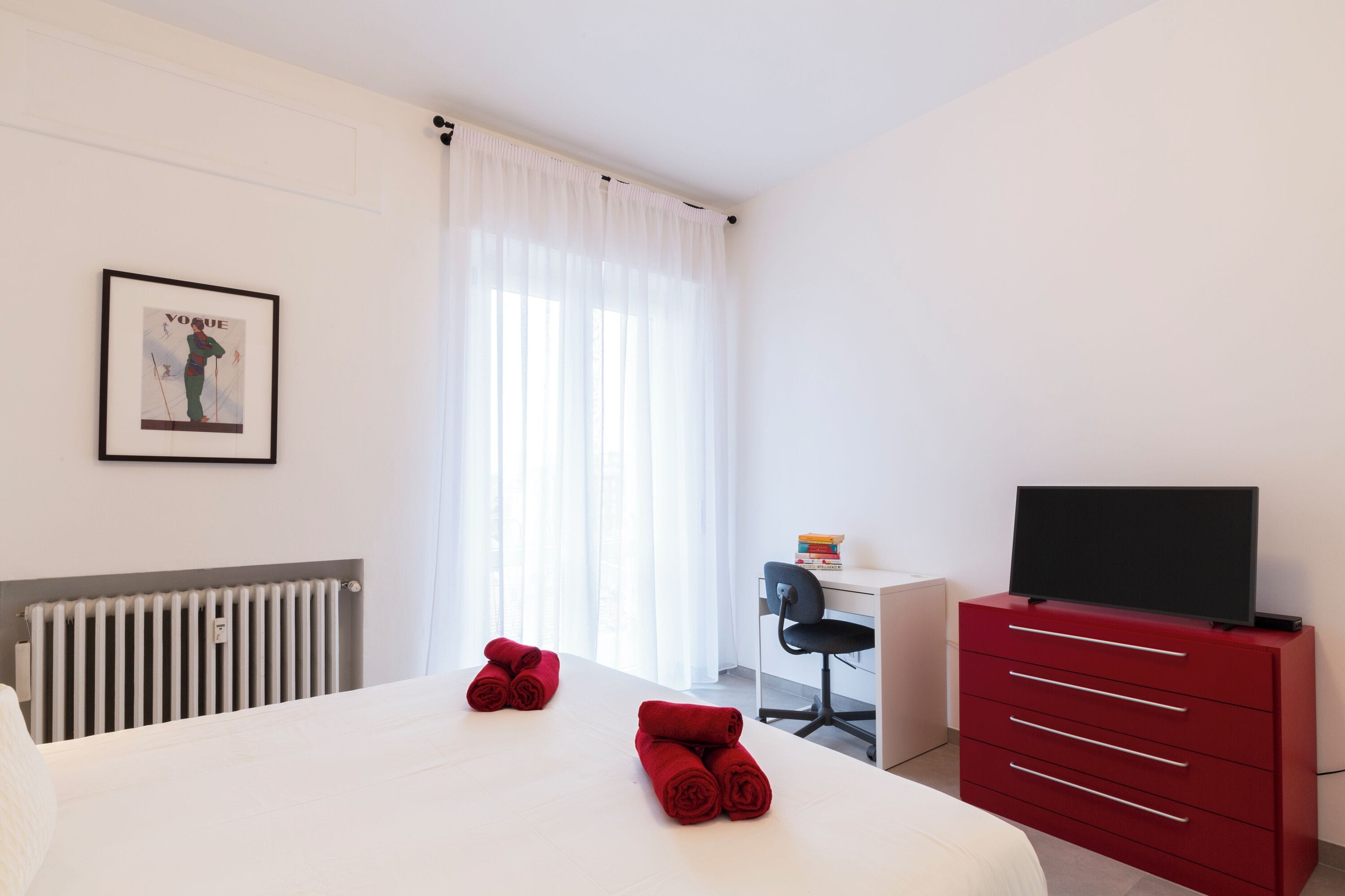 Quarto de hotel com cama, escrivaninha, cadeira, televisão e radiador.