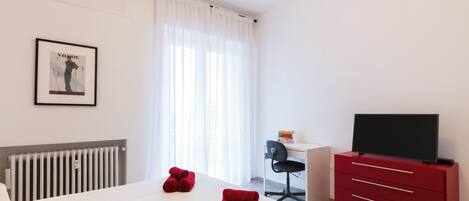 Quarto de hotel com cama, escrivaninha, cadeira, televisão e radiador.