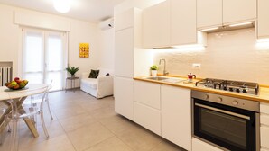 Eine moderne Küche mit weißen Schränken, einer Holzarbeitsplatte und einem Gasherd. Es gibt eine Essecke mit Tisch und Stühlen, und eine kleine Pflanze auf einem Beistelltisch.