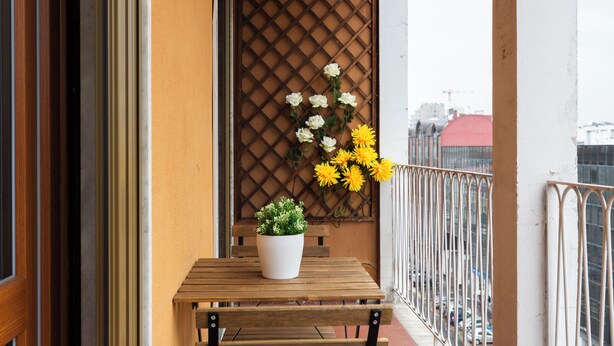 Ein Balkon mit Holztisch, Topfpflanze und Blumenarrangement.