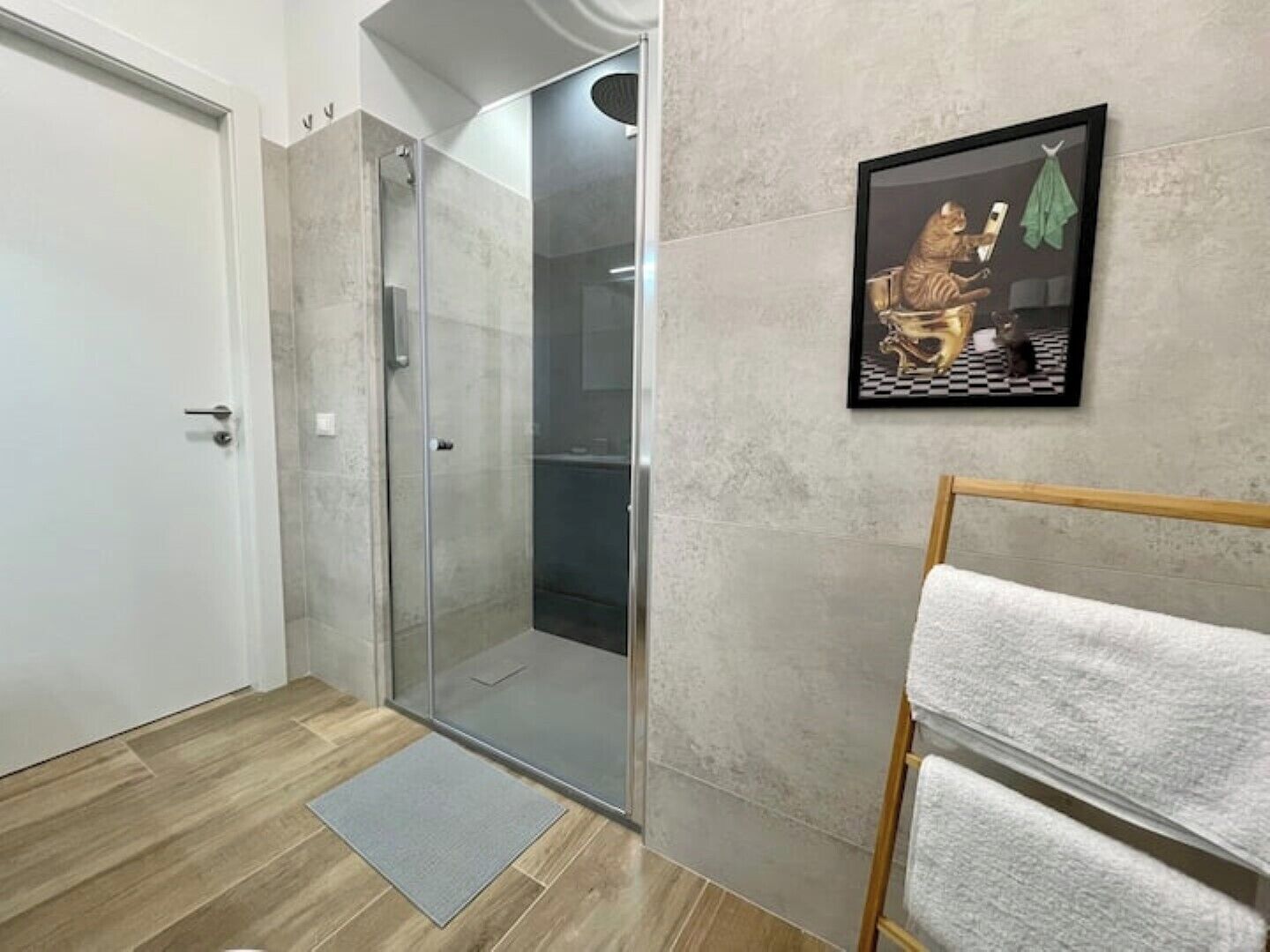 A bathroom with a glass shower enclosure, a towel rack, and a framed artwork on the wall.