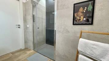 A bathroom with a glass shower enclosure, a towel rack, and a framed artwork on the wall.