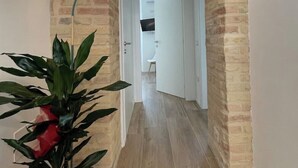 Un couloir aux murs en briques apparentes, avec un lampadaire vert et une plante en pot.
