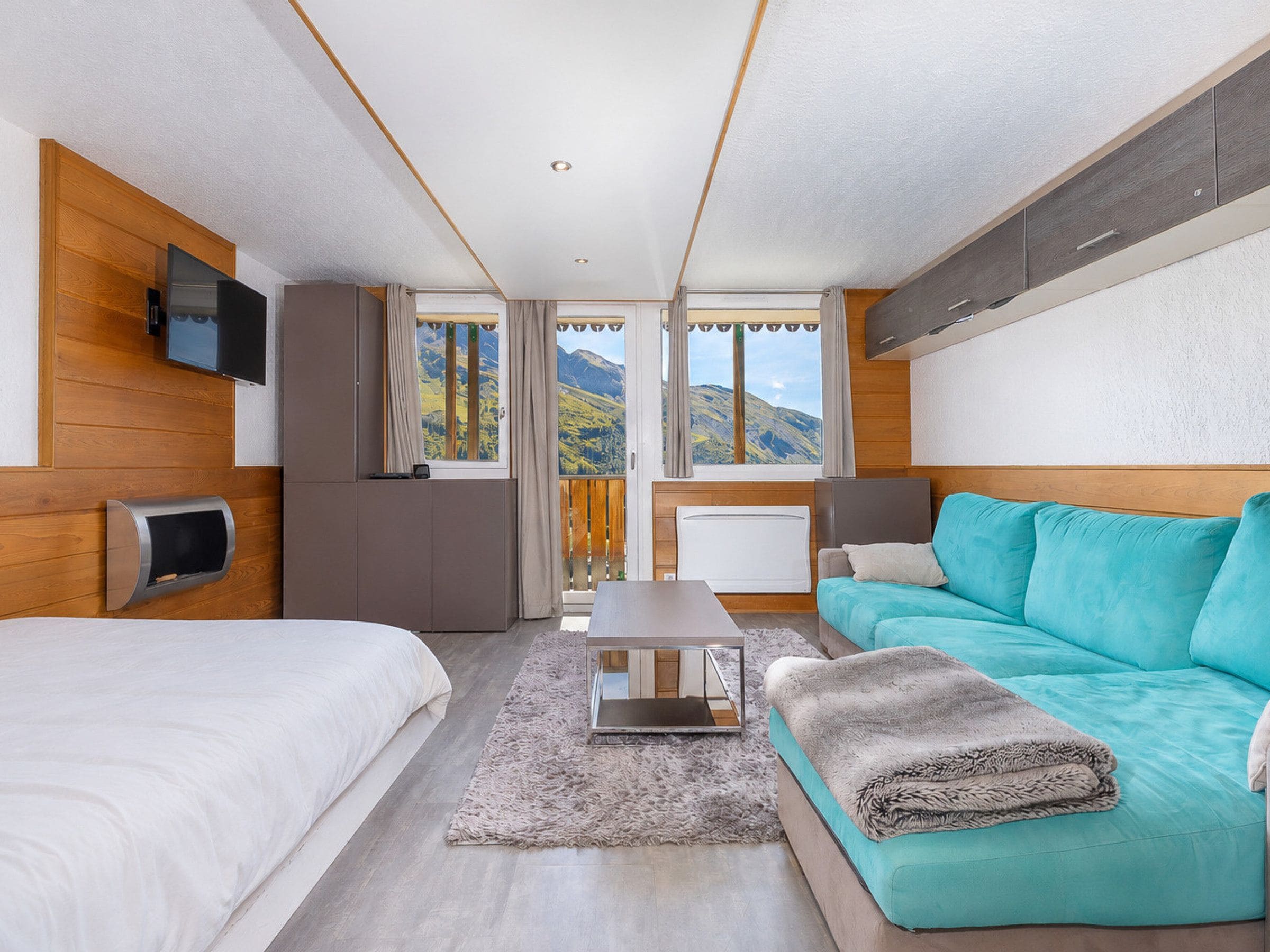 Une chambre moderne avec un lit, un canapé, une télévision et une vue sur les montagnes.