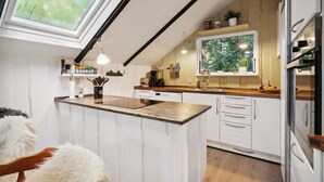 Une cuisine moderne dotée d’un îlot central, de plans de travail en bois, de meubles blancs et d’une grande fenêtre qui laisse entrer la lumière naturelle.