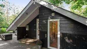 Un bâtiment en bois sombre, doté d’un toit en pente, d’un porche abrité et d’une grande fenêtre.