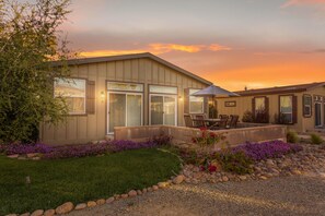 A modern house with a patio, large windows, and a well-maintained garden with purple flowers. - Ranch House View+Tub - 4 bedroom, 4 bath home on-site of Galway Downs (Temecula)