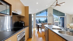 A modern kitchen with stainless steel appliances, wooden cabinets, and a large window offering a view of the outdoors. - Blue Bayou in Coronet Bay (Coronet Bay)