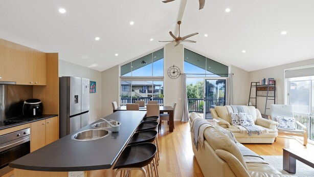 A modern kitchen with a central island, a dining area with chairs, a sofa, and a balcony with a view. - Blue Bayou in Coronet Bay (Coronet Bay)