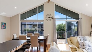 A spacious living area with a dining table and chairs, a sofa, and a large window offering a view of the outside. - Blue Bayou in Coronet Bay (Coronet Bay)