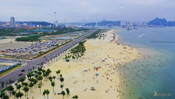 A beach with a long promenade lined with palm trees, a parking lot, and a view of the sea and distant mountains. - Villa Royal Lotus Ha Long (Hạ Long)