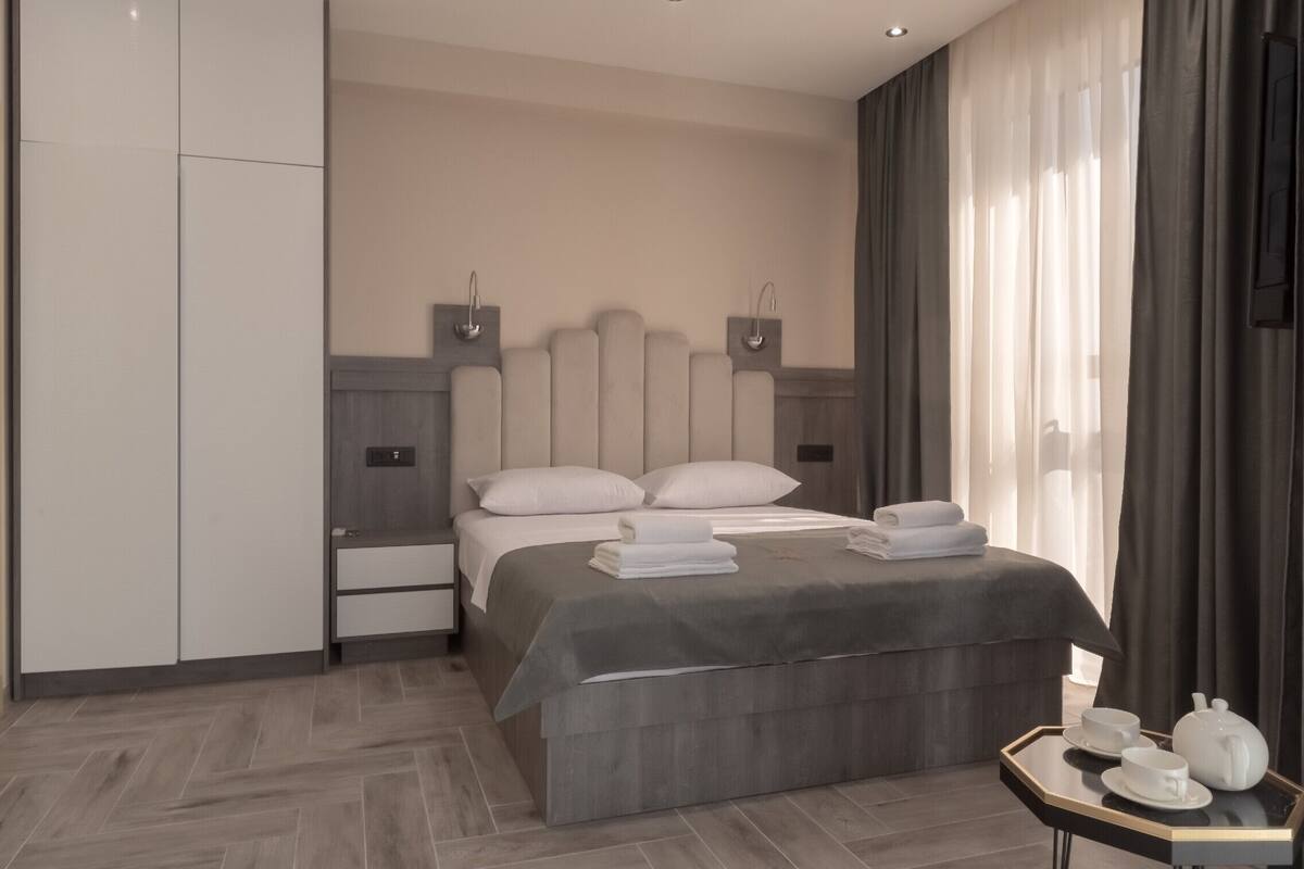 Ein modernes Hotelzimmer mit einem großen Bett, Nachttischen, einem Kleiderschrank und einem kleinen Tisch mit Tee-Zubehör.