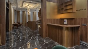 Zona de recepción de hotel con piso de mármol, mostrador de madera y cartel de recepción.