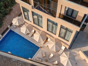 A modern building with a swimming pool, multiple windows, and outdoor seating with umbrellas. - Hotel Diman (Bar)