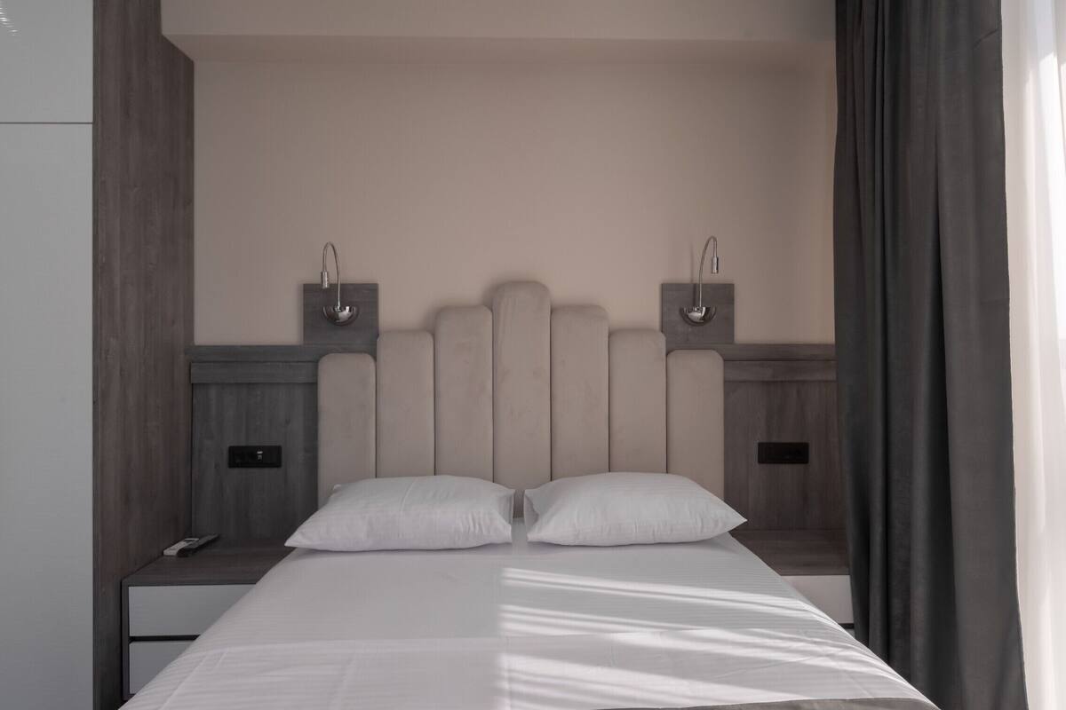 Ein modernes Hotelzimmer mit einem großen Bett, zwei Nachttischen und einem Kopfteil mit integrierter Beleuchtung.
