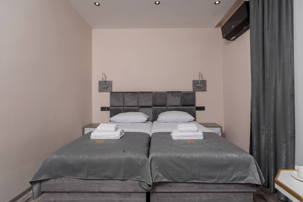 Ein modernes Hotelzimmer mit einem Doppelbett, zwei Nachttischen, einem kleinen Schreibtisch und einem großen Fenster mit Vorhängen.
