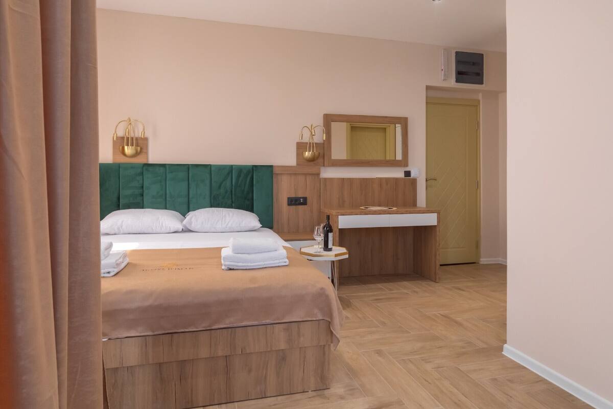Ein Hotelzimmer mit einem Bett, einem Nachttisch mit Flasche und Gläsern, einem Spiegel und einem Holzschrank.