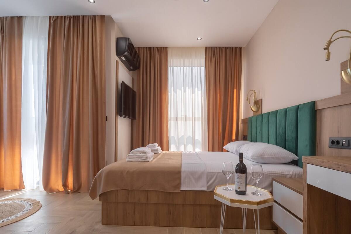 Ein Hotelzimmer mit einem Bett, einem Nachttisch mit Flasche und Gläsern, einem Fernseher an der Wand und Vorhängen.