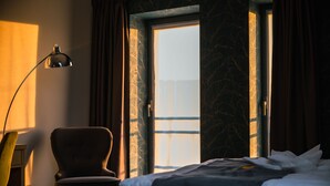 Una habitación de hotel con una cama, una silla, un escritorio y un ventanal con cortinas.