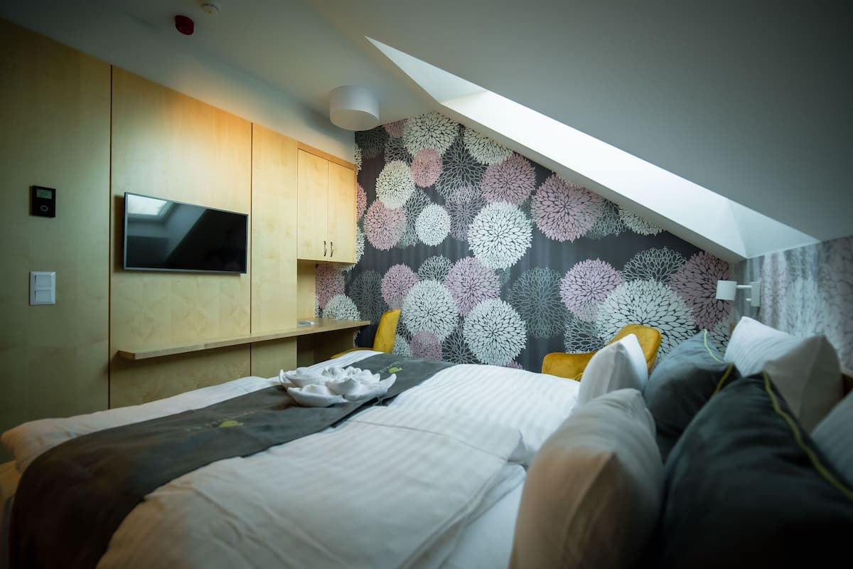 A modern bedroom with a flat-screen TV, wooden cabinets, a patterned wall, and a skylight.