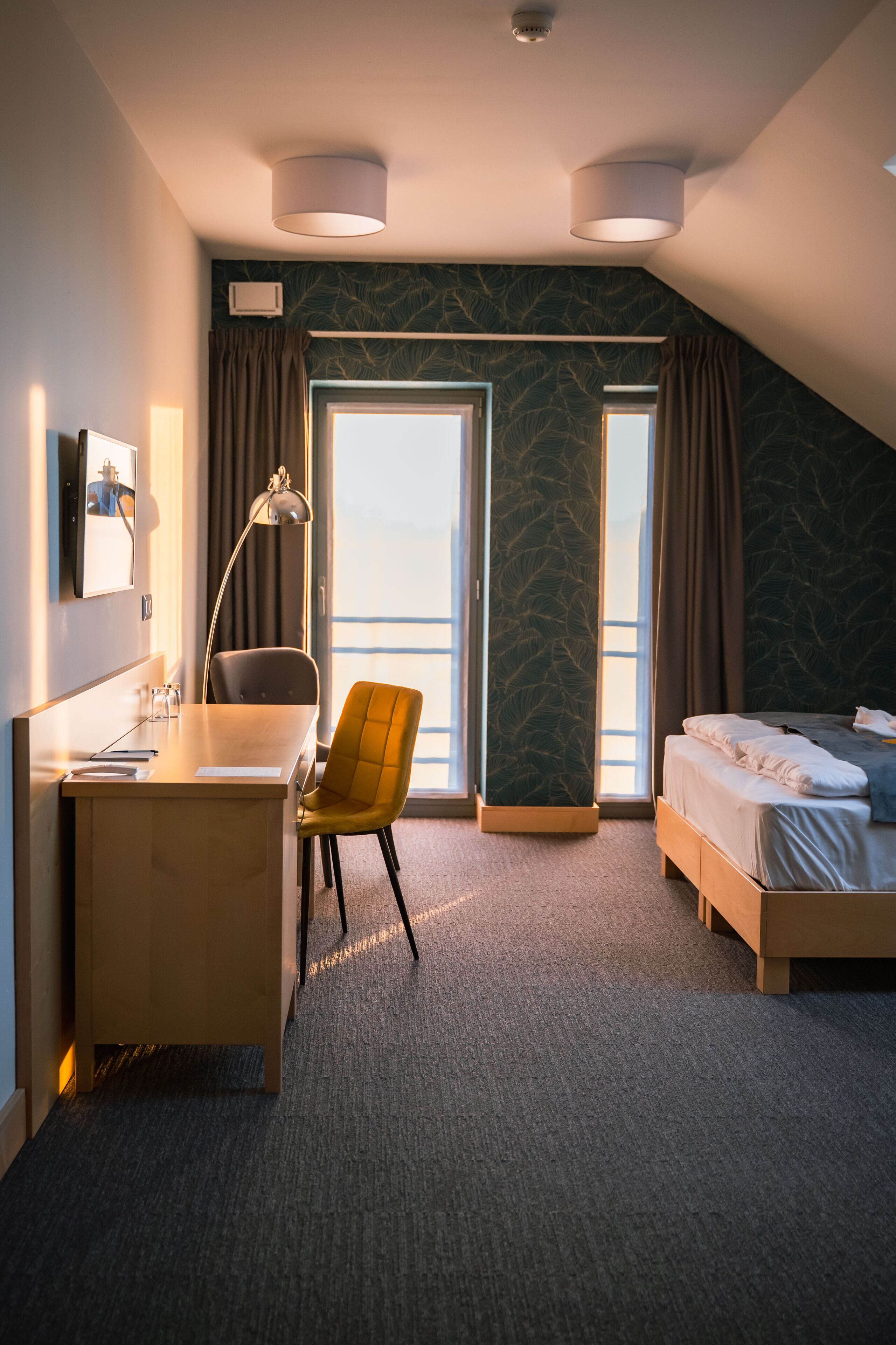 Habitación de hotel con escritorio, silla, cama y ventanas amplias.