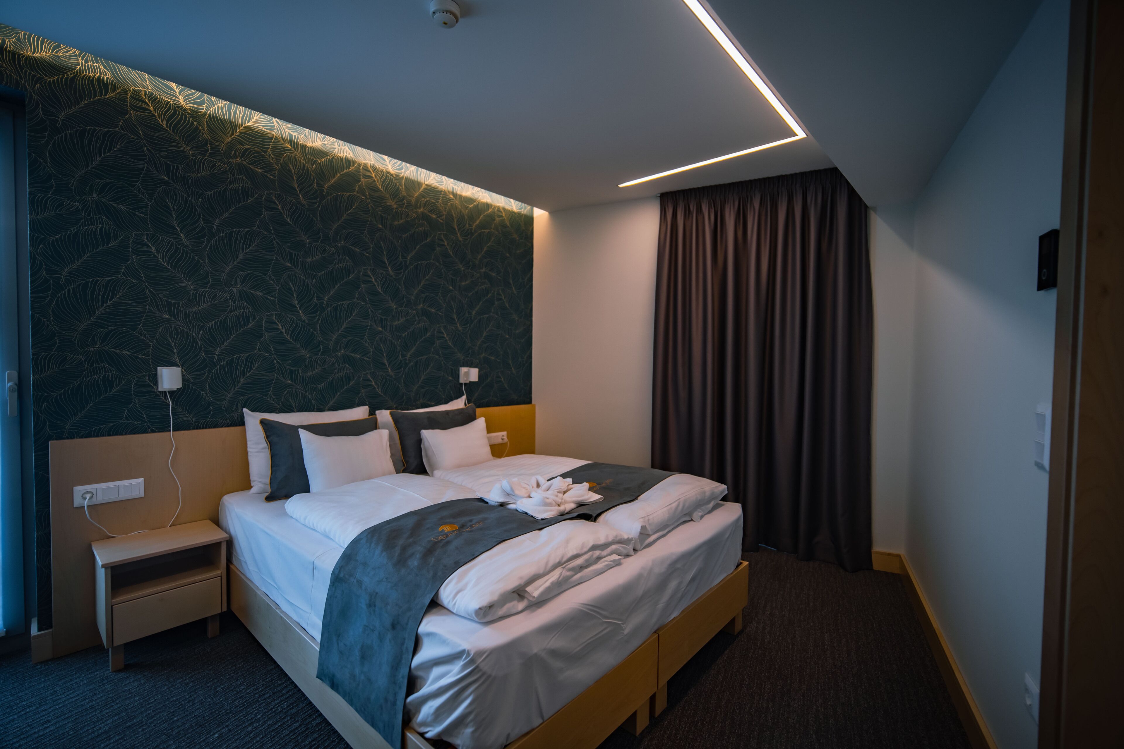 Habitación de hotel con una cama grande, una mesita de noche, una lámpara de pared y una cortina.