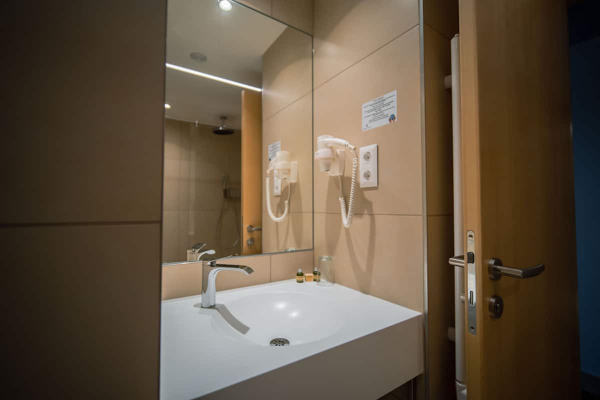 A modern bathroom with a white sink, a mirror, and a hairdryer mounted on the wall.