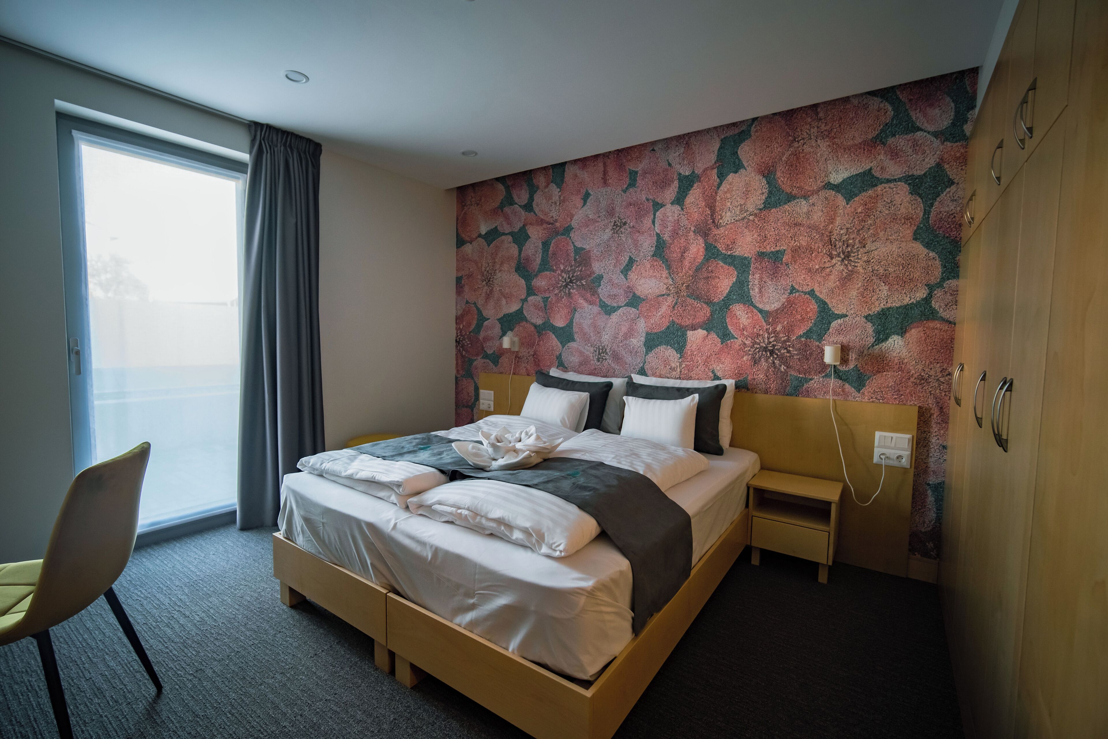 A hotel room with a large bed, a bedside table, a chair, and a window with curtains.