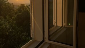 Ein Zimmer mit großem Fenster, Blick auf den Sonnenuntergang und einem Balkon mit Geländer.