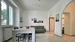Ein geräumiger Wohnbereich mit Esstisch und Stühlen, einem grauen Sofa und einem großen Fenster, das für natürliches Licht sorgt.