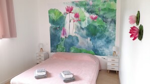 Une chambre avec un grand décor mural représentant des fleurs de lotus roses, une couvre-lit rose, deux tables de chevet avec des lampes et un rideau rose.