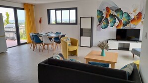 Un salon moderne comprenant un canapé, une table basse, un téléviseur et un coin repas avec des chaises et une table dressée pour six personnes.