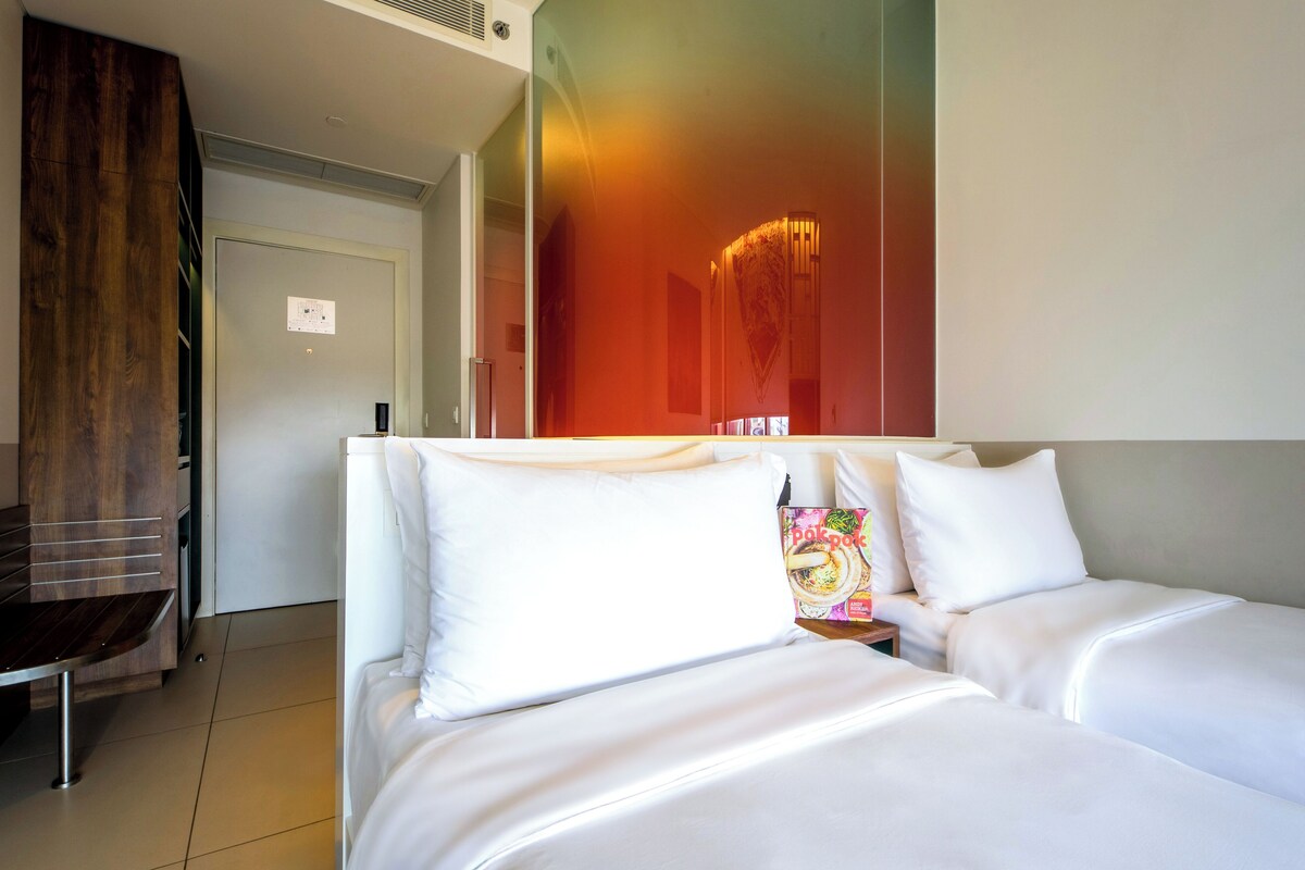 Een hotelkamer met een bed, een houten bank en een muur met kleurrijke kunst.