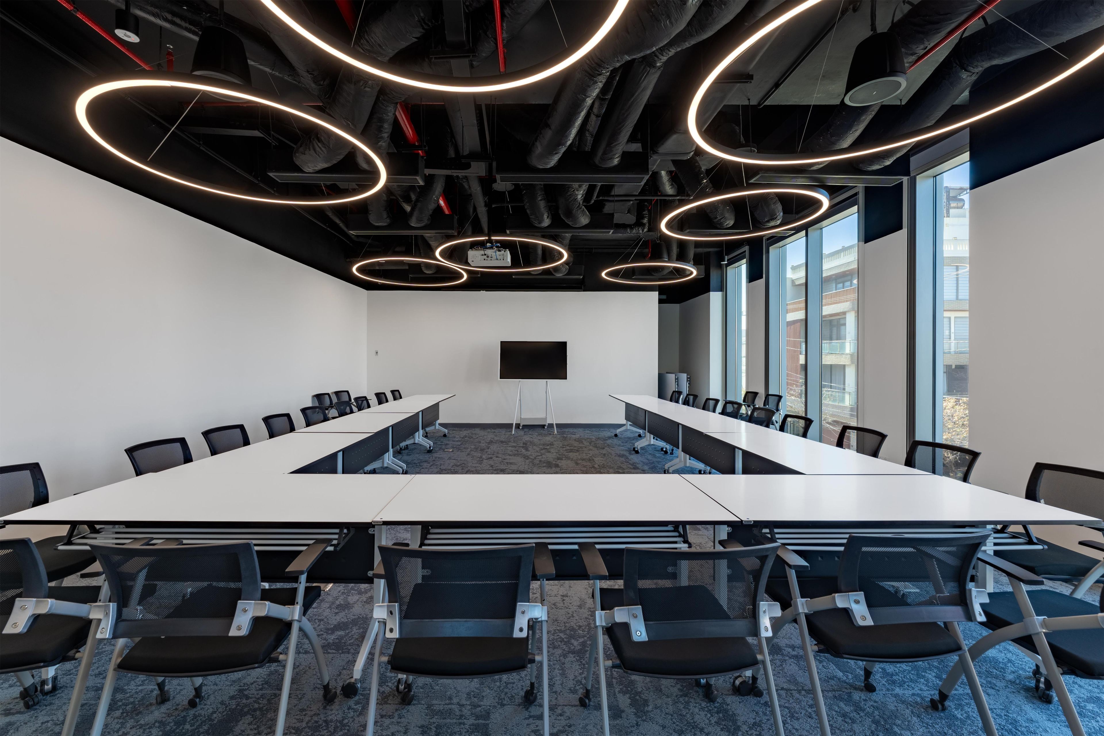 Une salle de conférence équipée d’une longue table, de chaises, d’un écran de projection et de grandes fenêtres.