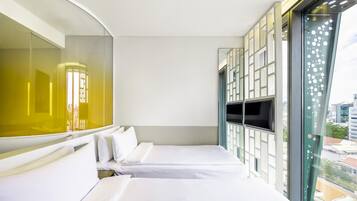 A hotel room with two beds, a large window with a view of buildings, and a mirrored wall.
