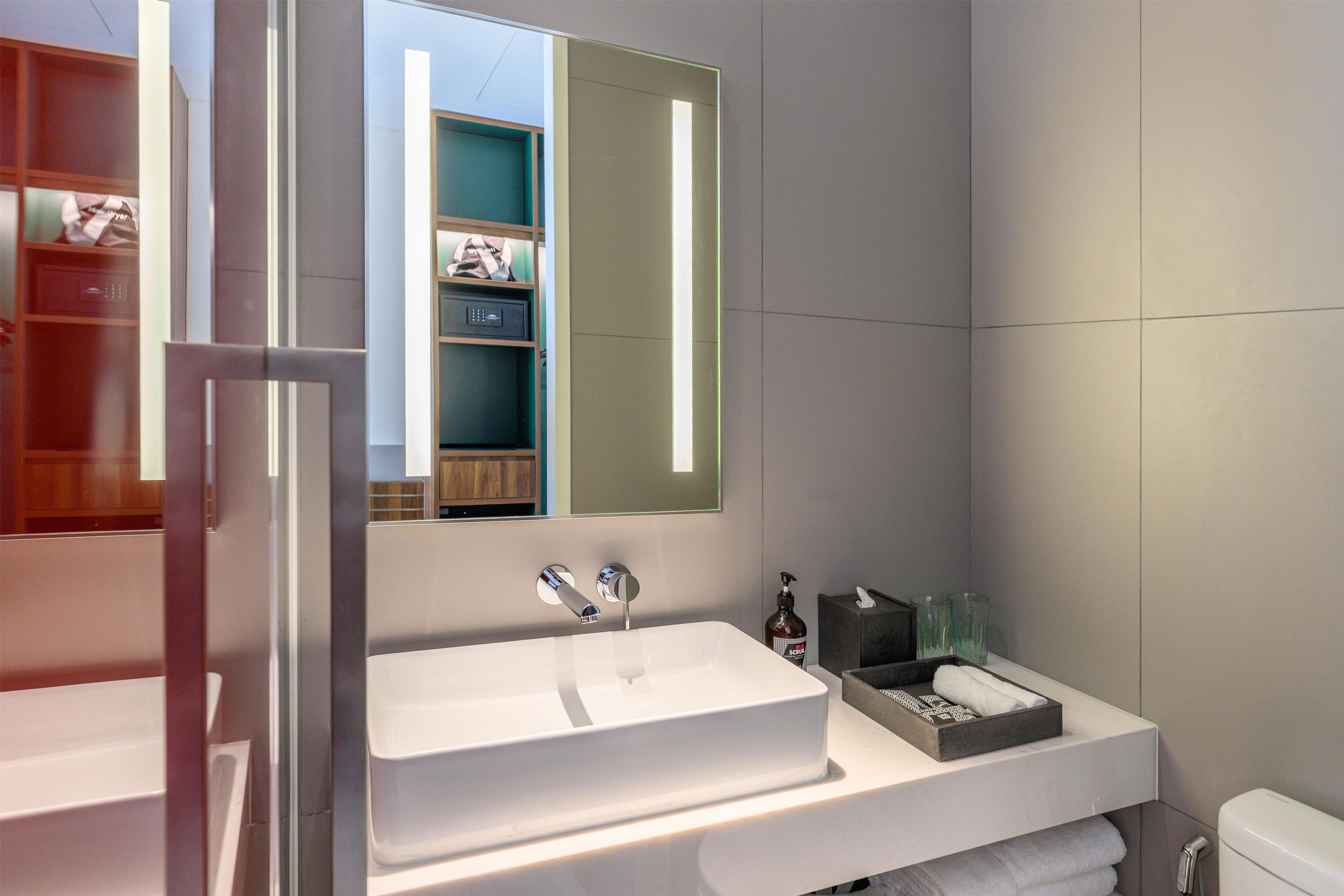 A modern bathroom with a large mirror, a white sink, and a toilet.