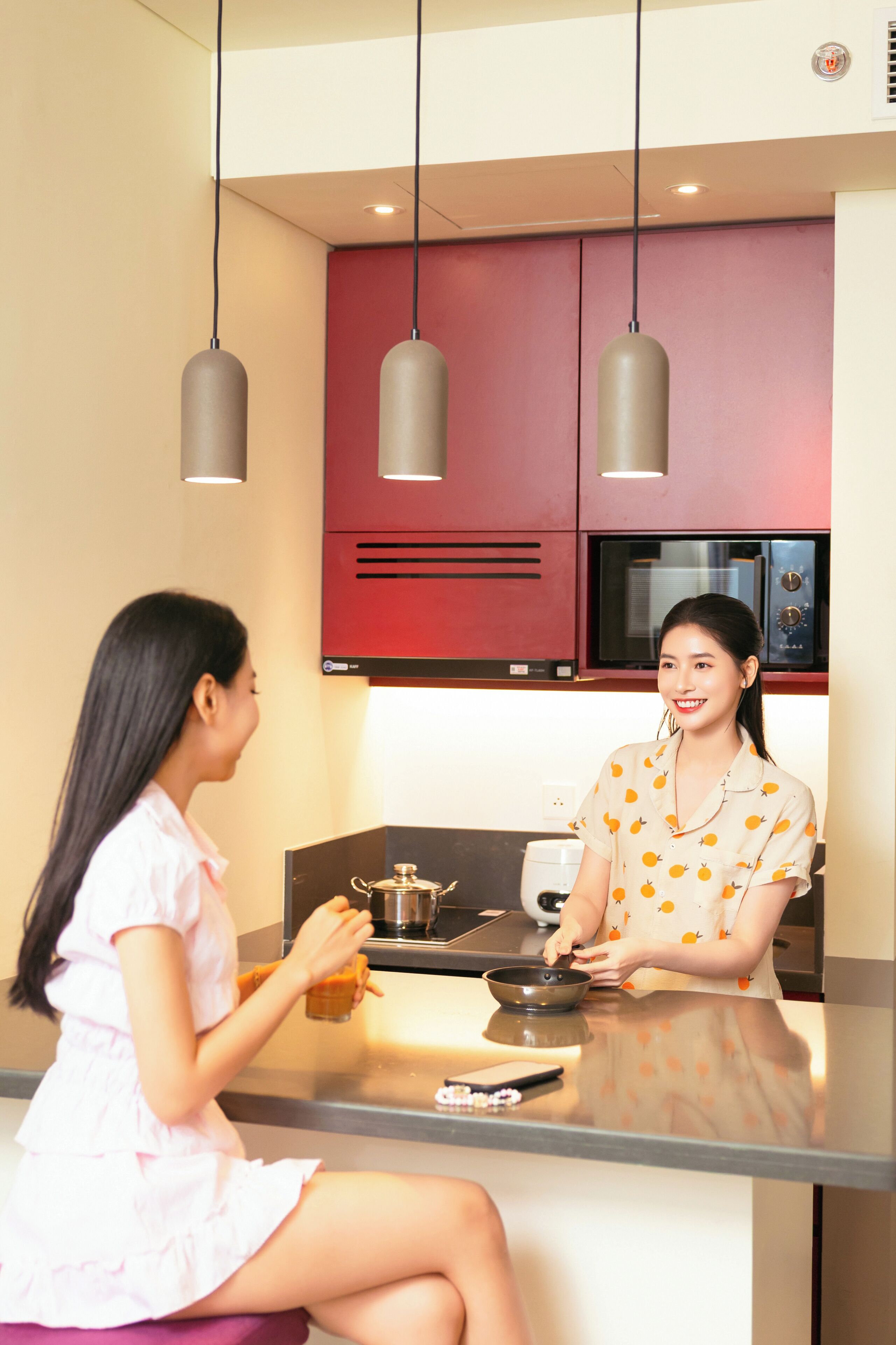 A modern kitchen with red cabinets, a microwave, and hanging pendant lights.