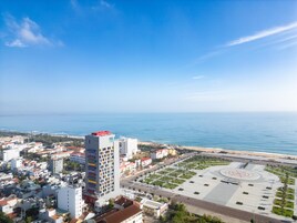 Un paisaje urbano costero con un edificio blanco destacado de techo rojo, una amplia plaza abierta con diseño circular y vista al mar.