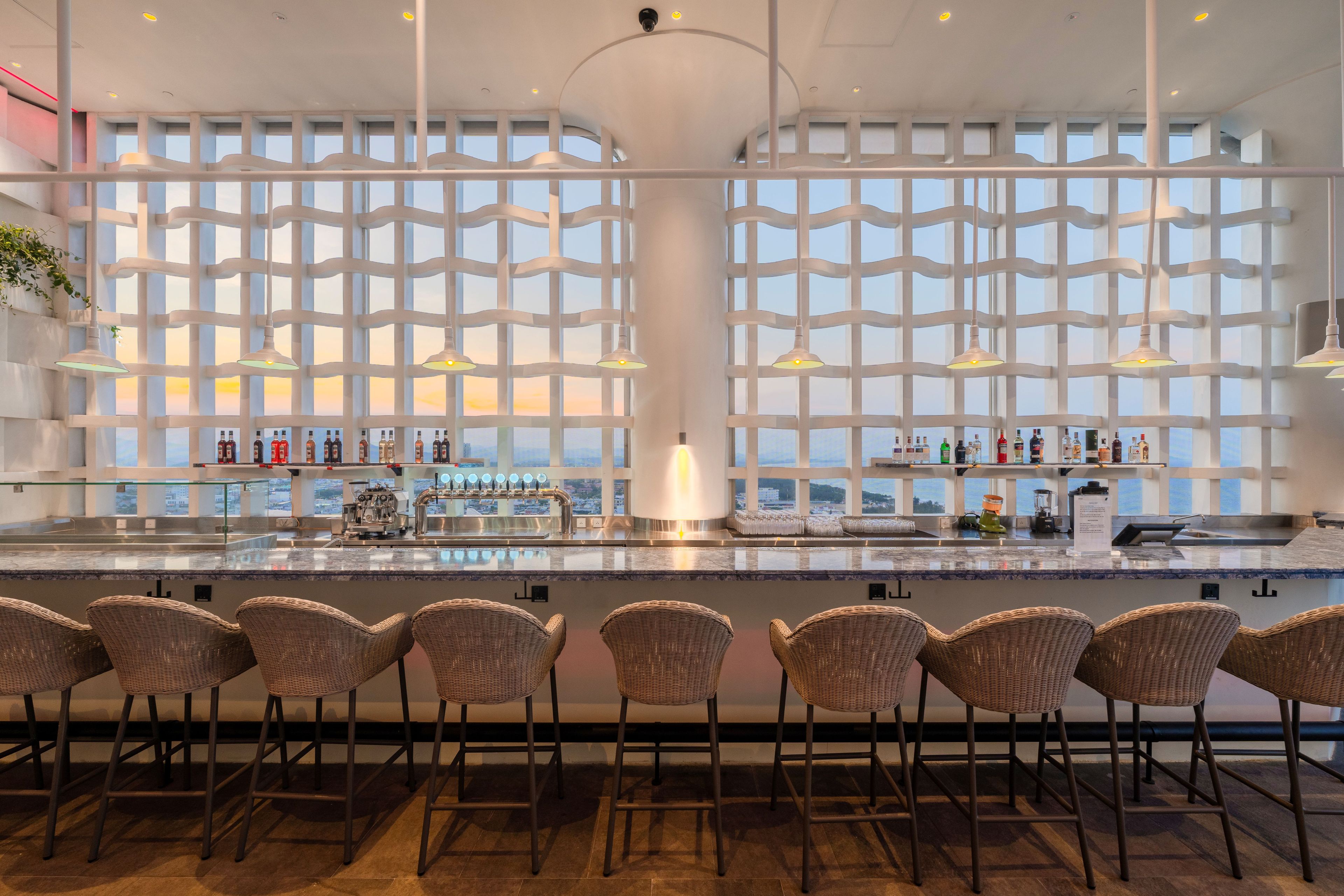 A bar area with a long counter, multiple bar stools, and a view through a patterned window.