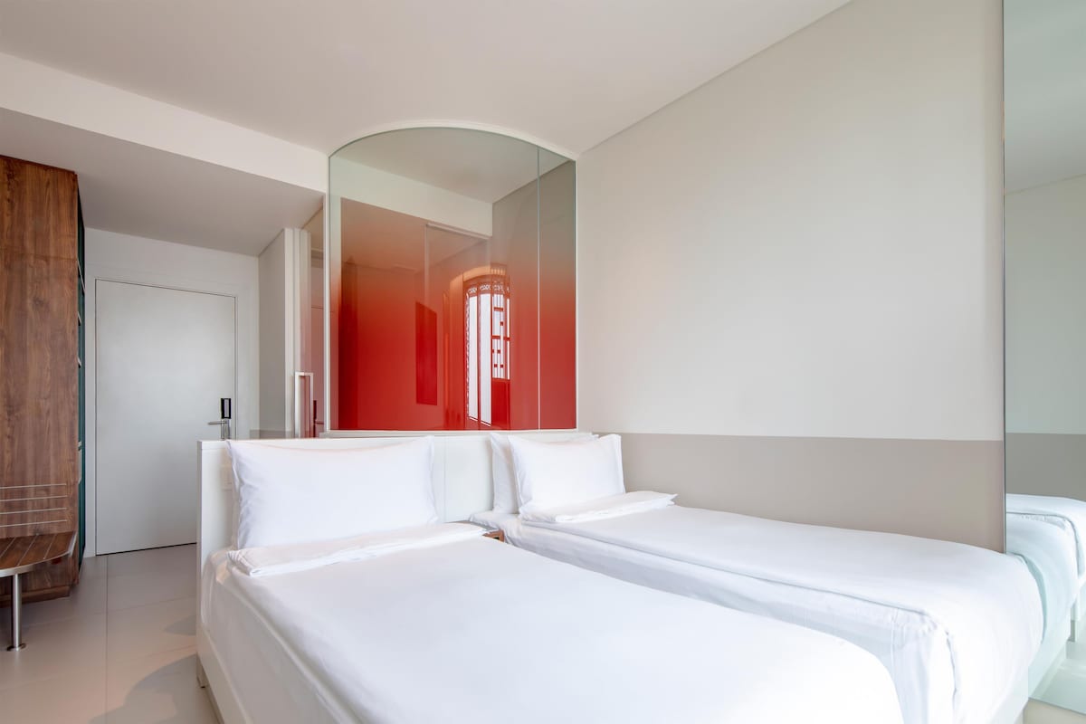 Ein modernes Hotelzimmer mit zwei Betten, einer Holzbank und einer roten Akzentwand.