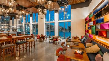 A spacious cafe with high ceilings, hanging wicker light fixtures, and a view of the cityscape through large windows.