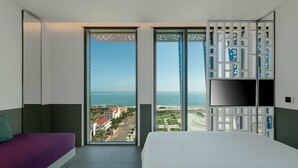 A hotel room with a large bed, a sofa, and a TV. The room has a view of the sea and a cityscape. - Wink Tuy Hoa Beach, Unscripted by Hyatt - 24 Hours stay (Tuy Hoa)