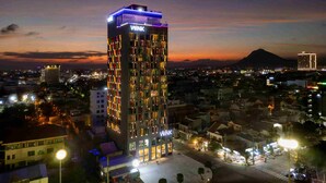 A tall hotel with a 'WINK' sign, surrounded by a cityscape at dusk. - Wink Tuy Hoa Beach, Unscripted by Hyatt - 24 Hours stay (Tuy Hoa)