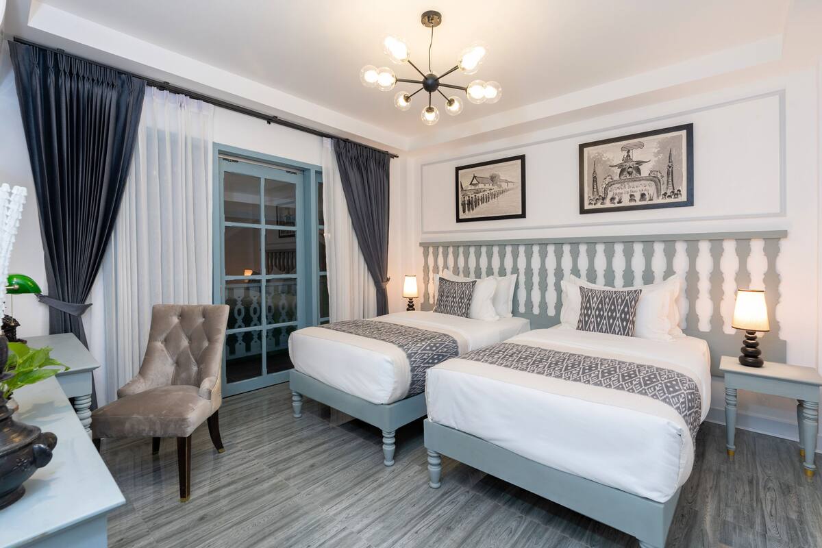 Ein Hotelzimmer mit zwei Betten, einem Sessel, einem Schreibtisch und einem Fenster mit Vorhängen.