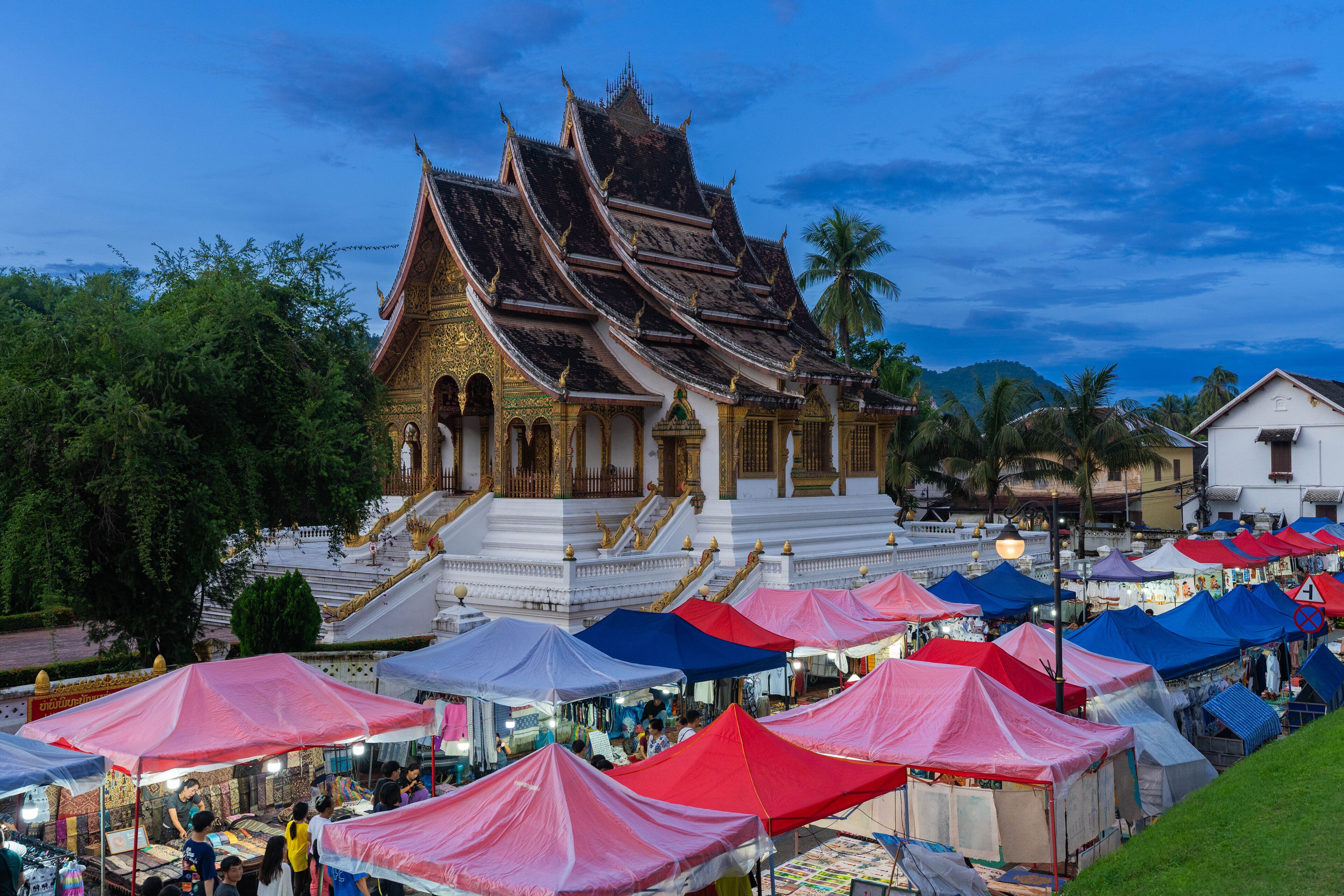 A traditional Thai temple with ornate architecture, surrounded by a market area with colorful tents.